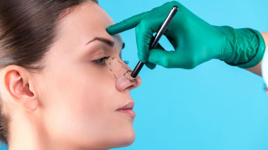 Gloved surgeon using a caliper to measure nasal shape during a pre-rhinoplasty assessment.