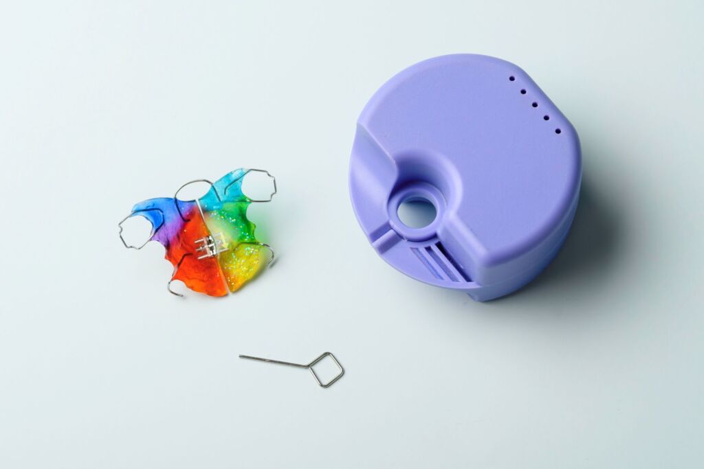 Colorful removable orthodontic retainer placed next to a purple storage case on a clean surface