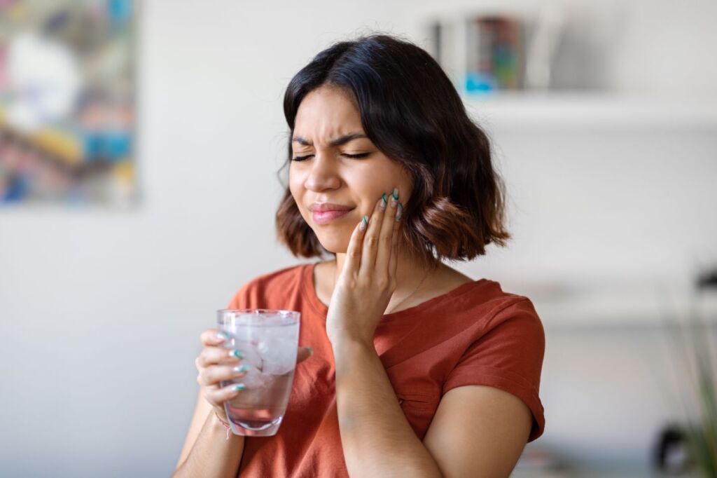 Woman touching her cheek while holding a glass to show tooth sensitivity or pain